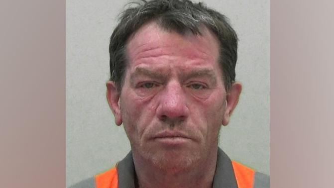 A mugshot of Gordon Grieveson. He brown hair which is greying and is wearing an orange hi-vis jacket.