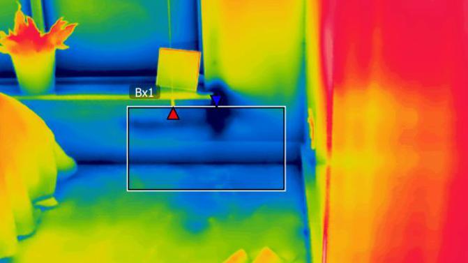 A heat loss map of the corner of a bedroom with patches in different colours - blue areas  - showing cooler temperatures - appear around the room's window and wall