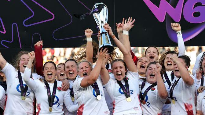 England women's team celebrate, holding up a trophy