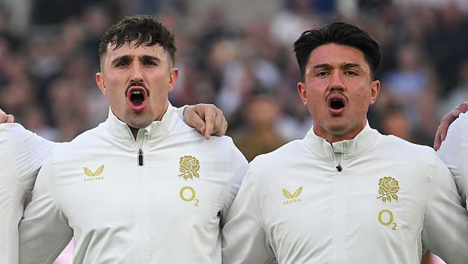 Caden Murley (left) and Marcus Smith stand in a line with their arms around each other singing the national anthem before England v France