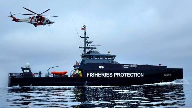 The black and grey Falklands fisheries protection vessel - Lilibet - with a red and white helicopter flying above it. The words Fisheries Protection are written in large letters down the side.