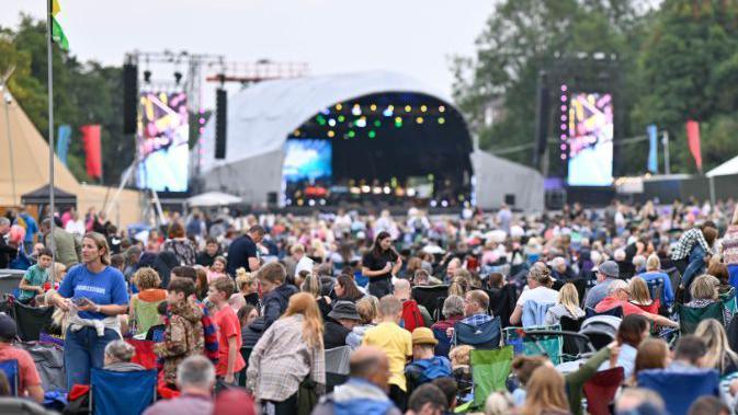 A sea of people - many sitting in camping chairs looking towards a stage.