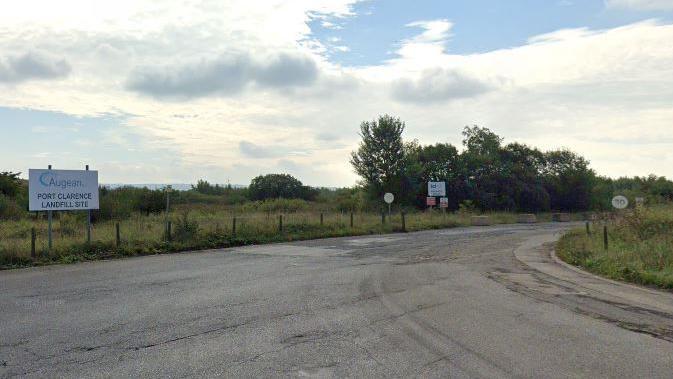 Entrance road leading to Augean at Port Clarence. There is a small white sign with the firm's name on it on the left-hand side of the road. The road is Tarmac and has a 30mph speed limit. It is surrounded by grassed areas and trees.
