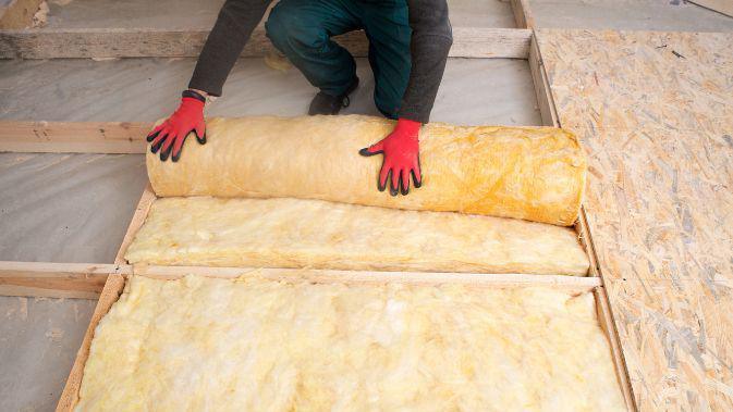 A man installing some loft insulation. He is wearing red gloves.