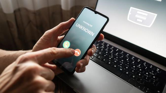 A stock photo of a person answering an unknown call, with a laptop in the background.
