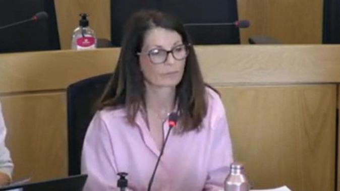A woman with straight long brown hearing wearing glasses and dressed in a pink shirt.