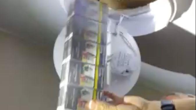 A multi-pack of illegal cigarettes being removed from where they were hidden in a roof space behind a light fitting. A hand wearing a watch is holding the multi-pack.