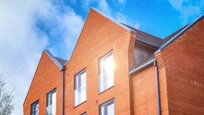 The roofs of two redbrick houses are visible with a blue sky in the background.
The sun can be seen in the reflection of second-storey window.