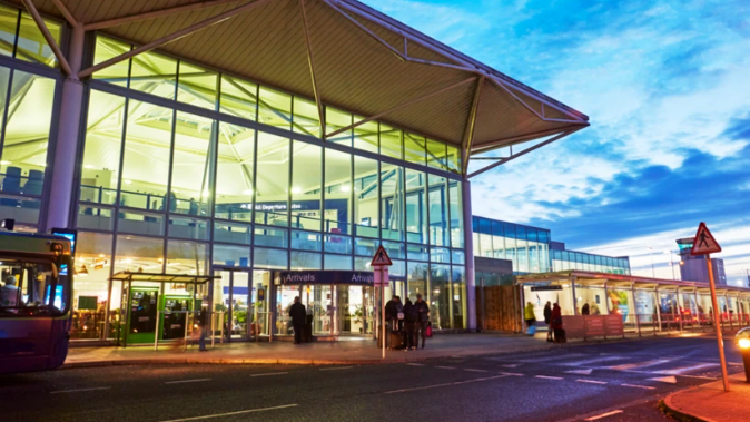 Bristol Airport. The building is modern and has many glass panels. There is a pedestrian crossing directly outside the entrance and there are people in and around the building.