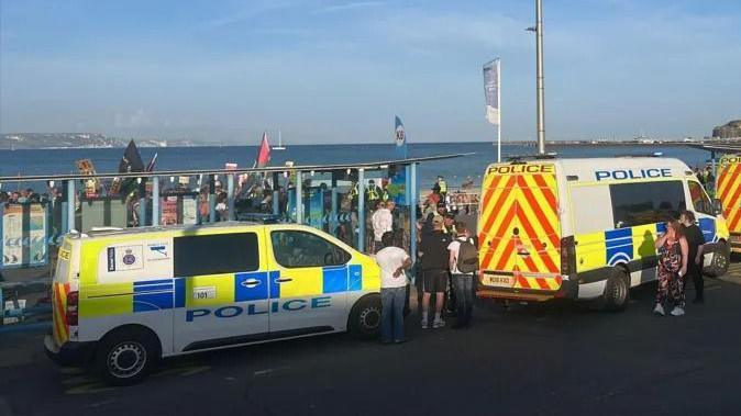 Police vans parked on Weymouth seafront near people with banners