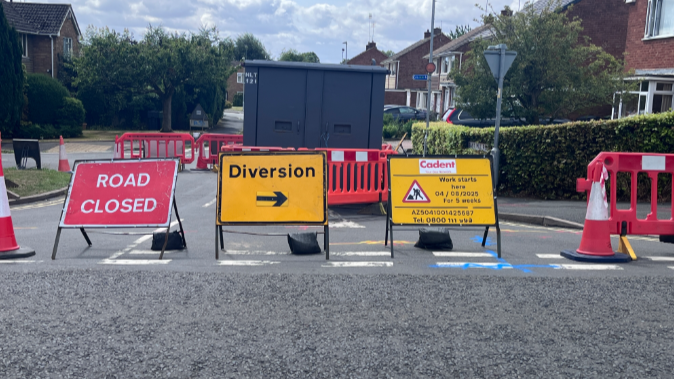Roadworks signs and road closed signs are in front a a road that is closed in the town warning of diversions