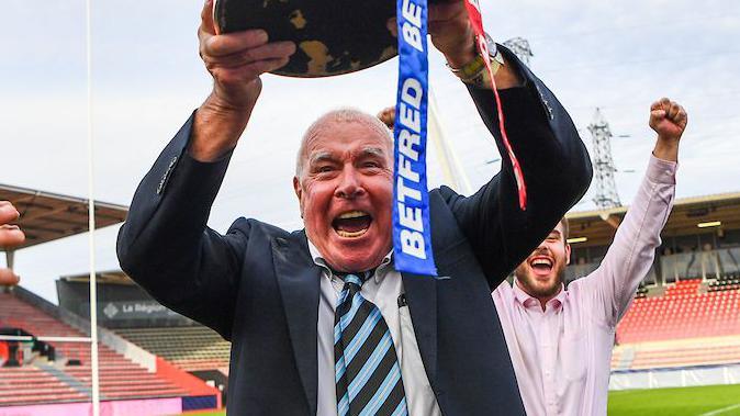 London Broncos owner David Hughes celebrating the club's return to Super League trophy by holding the Betfred Championship Trophy aloft in Toulouse.