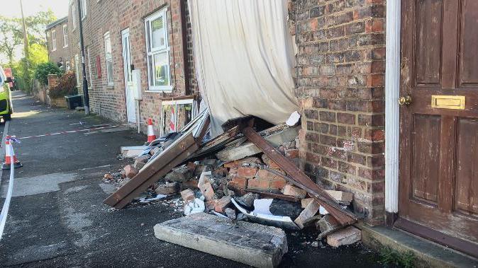A pile of bricks and windows lies next to a terraced house which has been damaged when a car drove into it.