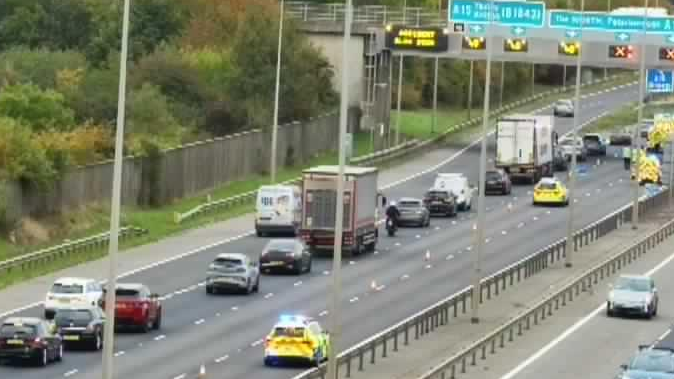 A traffic camera images showing slowing traffic on the A1 northbound. Traffic is queuing in the left hand lane. Police cars with flashing lights andother emergency vehicles are travelling on the other two lanes. 