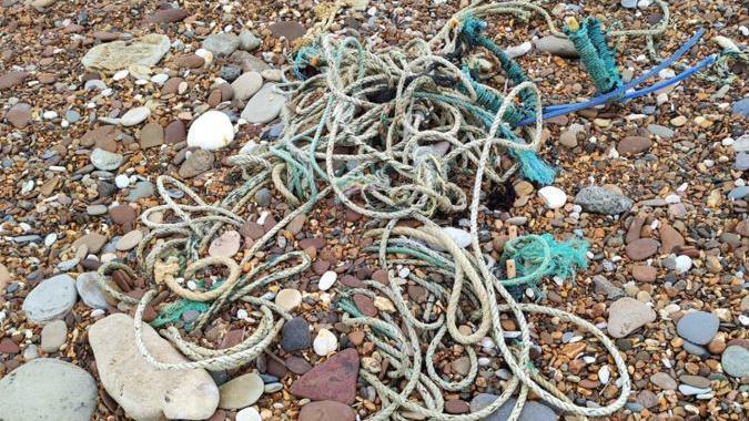 Dozens of different coloured, tangled ropes on a pebbly stone-filled beach. 