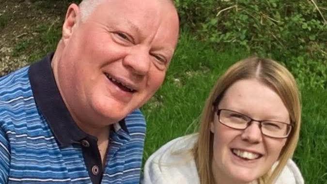 A man in a striped shirt smiles next to his daughter, who wears a grey hoodie.