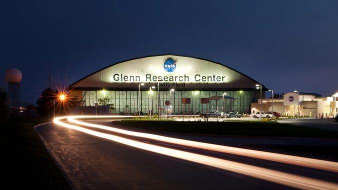 A hangar with Glenn Research Center written on the front. The photograph is taken at night with the building illuminated by lights. 