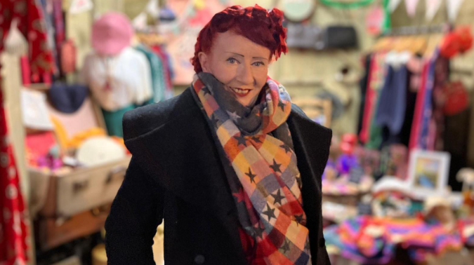 Shows a woman with red hair, a black overcoat and multi-coloured scarf