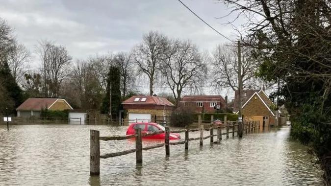 A flooded path and car park, with water half way up a car