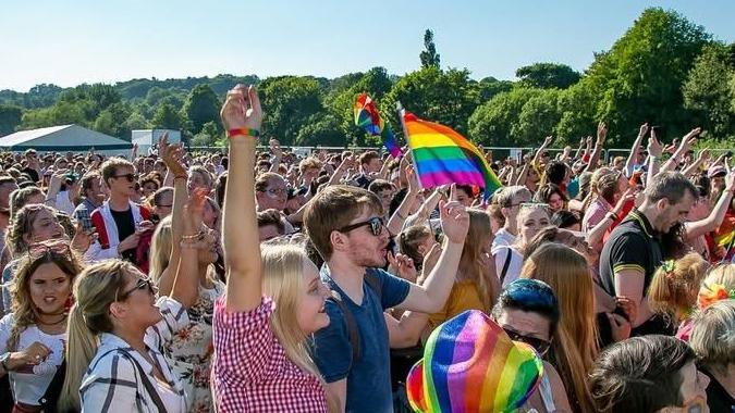 A crowd raising their hands in the air and waving rainbow Pride flags during a Pride event in Durham