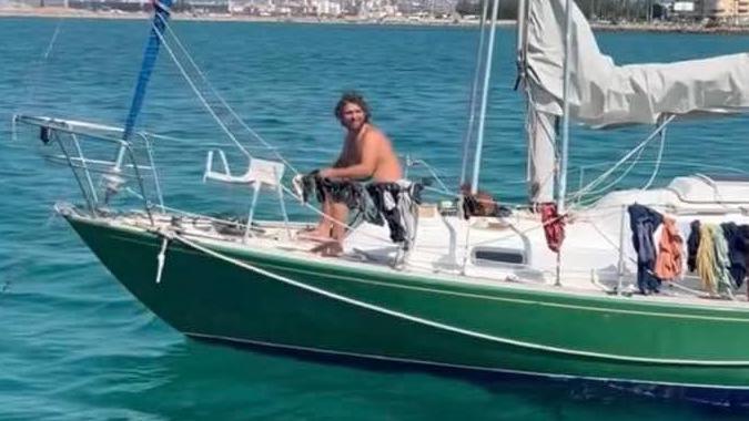 James Nunan sitting on the deck of his small green boat. He is topless and smiling while at sea.