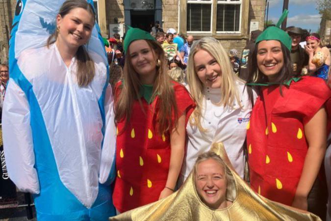 A group of young women in fancy dress standing outside a pub, one is dressed as a dolphin, others as strawberries