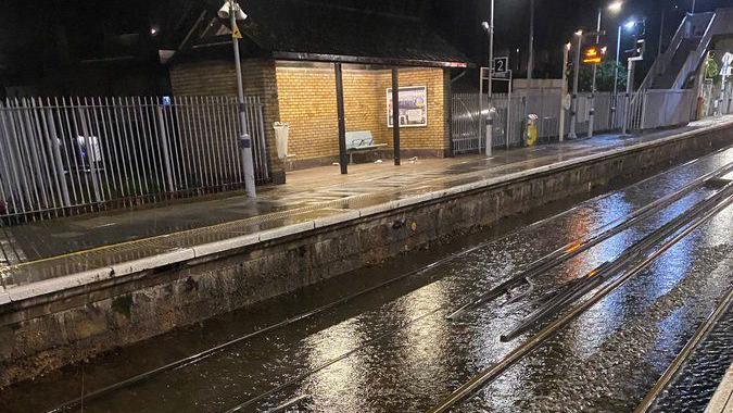 A flooded railway line seen with a platform in the background