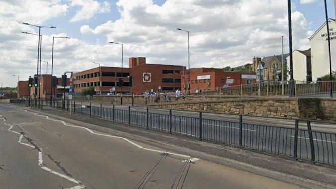 A Google Maps image of a dual carriage way with barriers segregating each road direction, and a brick building in the background.