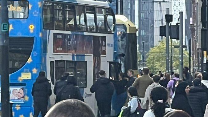 Large crowds of people gather around a bus and a tram that have collided on a street