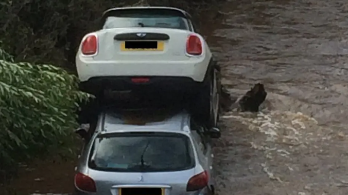 Two cars sat on top of each other surrounded by flood water