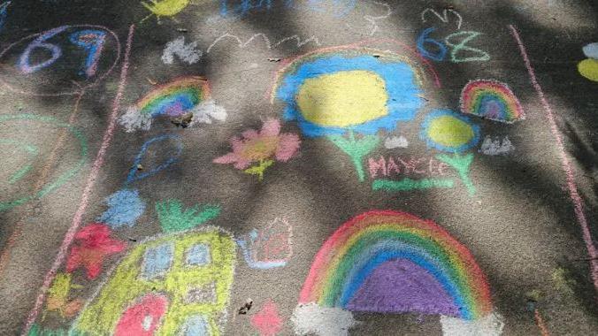 A drawing in different coloured chalk on a brown pavement. There is dappled light shining over the illustration