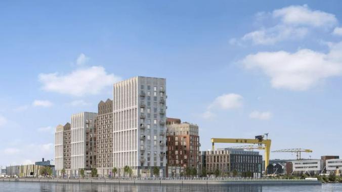 Apartments seen across a river. The Harland and Wolff cranes are along the skyline.