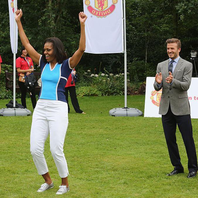 Michelle Obama puts her hands in the air and cheers, David Beckham is stood behind her