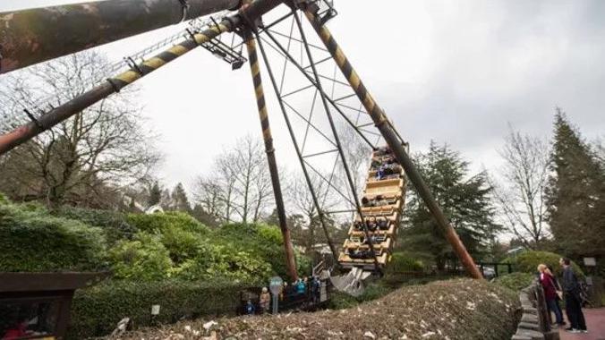 A wide shot of the ride, with two people stood watching as it swings. The ride comprises four large struts, with seating that rocks backwards and forwards.