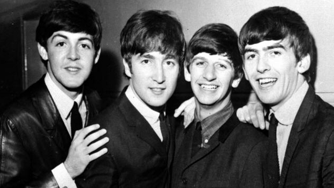 A black and white photo of the Beatles taken in 1965, showing, from l to r, Paul McCartney, John Lennon, Ringo Starr and George Harrison. Each is wearing a suit and tie and sporting the distinctive mop top haircut for which they were famous.