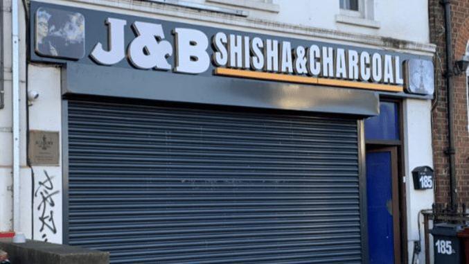 A shopfront with the words J&B Shisha & Charcoal printed in white on a black background above a closed metal roller shutter