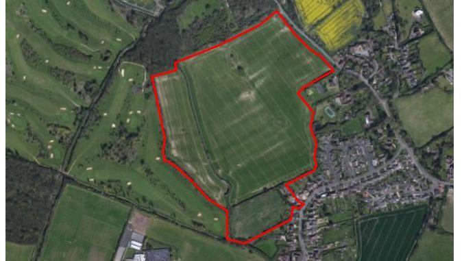 An aerial photo of land which is mostly fields and a golf course, with housing on one edge. The earmarked land is outlined in red.