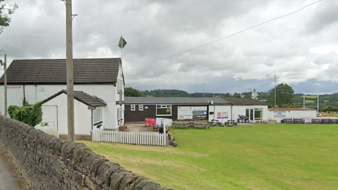 The outside of a sports club, where some clubhouses and picnic tables sit next to the edge of a sports pitch.