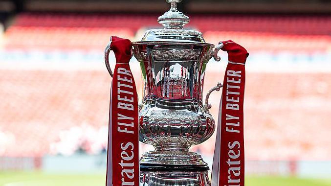The FA Cup trophy, with red ribbons containing the sponsor's name, at Wembley