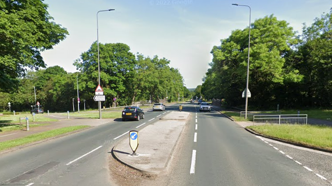 A Google Street View screen capture of the A18, it is a wide tree-lined A-road with cars travelling on it.