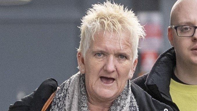 Mandy Wixon walking into Gloucester Crown Court. She has short, bleach-blonde hair and multiple ear piercings. She is in her late 50s. She has a black overcoat on and a grey scarf. A young, bald man in a black jacket and yellow jumper is walking behind her. 