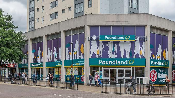 A two-storey concrete building containing a Poundland shop. Behind it is an office block.
