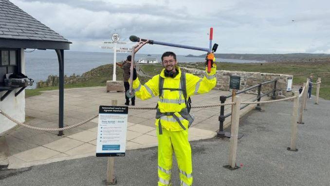 Harry in hi-vis holding his scooter over his head, smiling as he completes his journey. The Land's End sign is in the background.