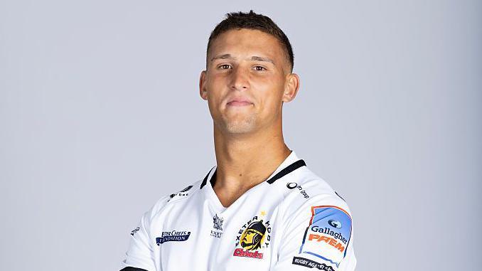 Harry Ascherl wearing Exeter kit standing with his arms folded looking at the camera