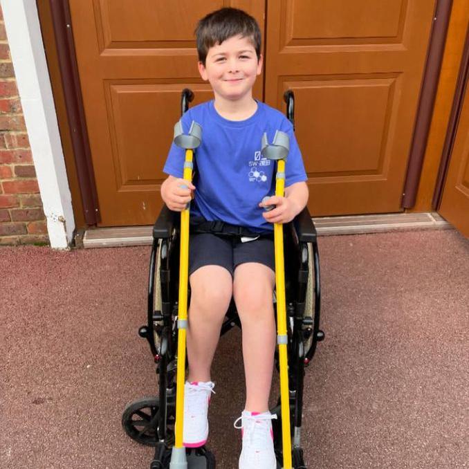 Harry is seen in a wheelchair smiling while holding a pair of yellow crutches. 