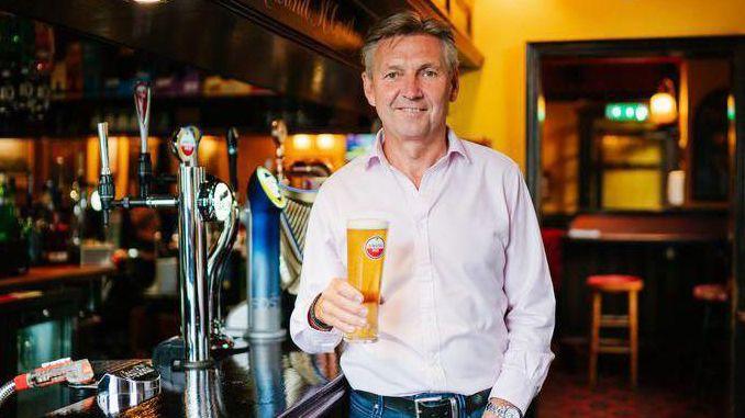 Phil Thorley, who runs the Thorley Taverns pub group, wears a white shirt and blue jeans as he leans against the bar holding a pint of Amstel.
