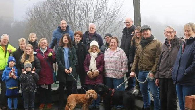 A group of people and two dogs are pictured on the site with the water tower in the faint, misty distance.