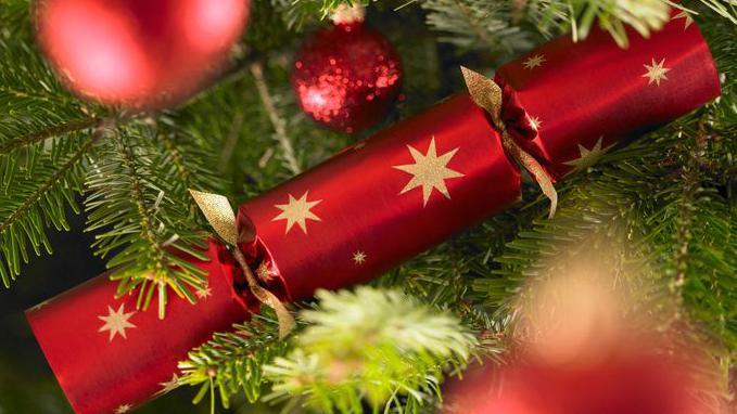A red Christmas cracker with gold foil star decoration is placed in a Christmas tree.