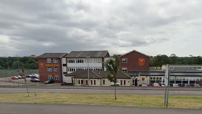 A Google street view screenshot of Netherhall School in Maryport. It is made up of several buildings, with a car park at the front and a sports pitch to the side.