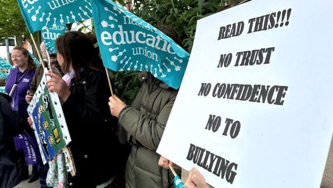 Protesters holding banners with one reading "Read this! No trust, no confidence, no to bullying"d